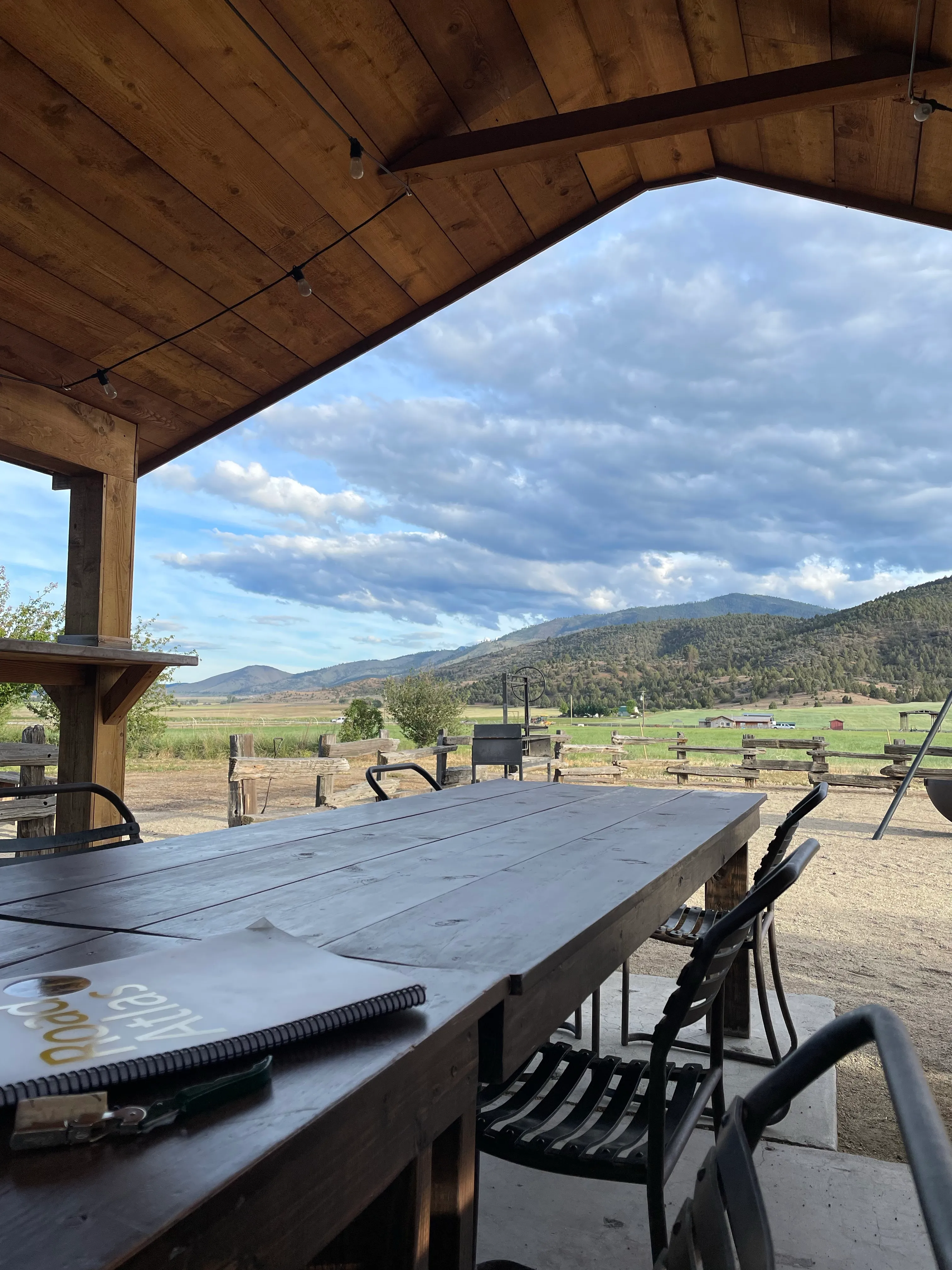 Wooded green hills in the distance, framed by a wooden structure. Far off farm accoutrements are visible, including a tractor and farm building.