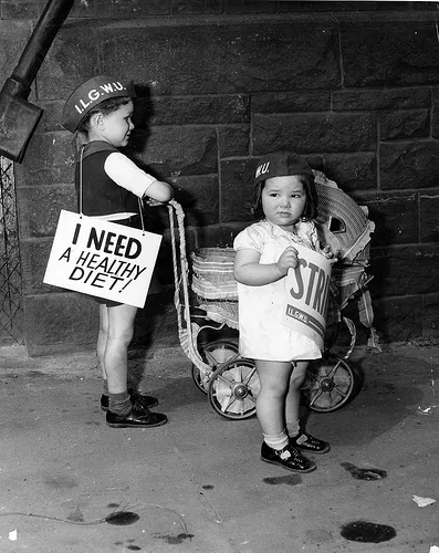 "Two young children picket for the ILGWU carrying placards including 'I Need a Healthy Diet!' outside the Kolodney and Myers Employment Office" by the Kheel Center at Cornell University, used under CC-BY 2.0.