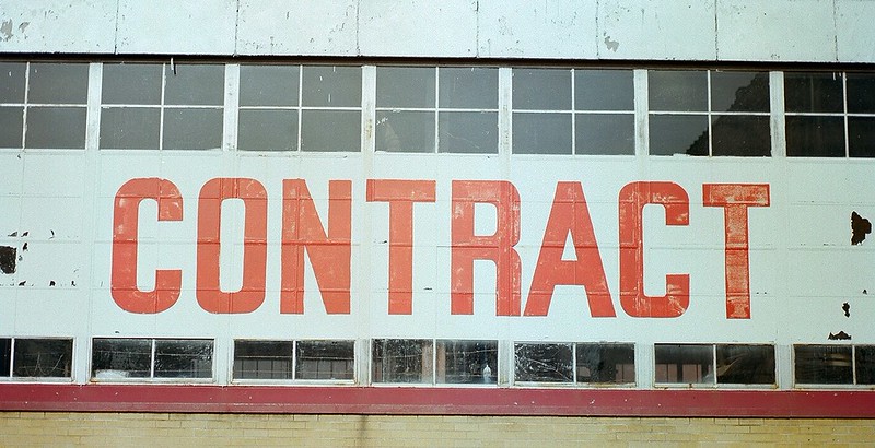 A wall with windows, perhaps of a warehouse, with giant, red, block letters reading CONTRACT